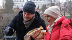 Na zdjęciu kobieta i mężczyzna w zimowych ubraniach. On ma ciemną kurtkę i czapkę, ona – czerwoną kurtkę i różową czapkę. Są uśmiechnięci, rozmawiają z kimś, kogo nie ma w kadrze. To aktorzy Kinga Preis i Artur Żmijewski, którzy grają główne role w  seria