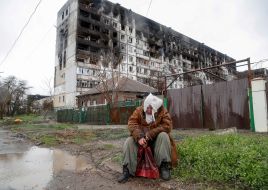 Женщина сидит перед жилым домом, поврежденным в ходе российского вторжения. Мариуполь, Украина. 13 апреля 2022 года. Фото: Александр Ермоченко / Reuters / Forum